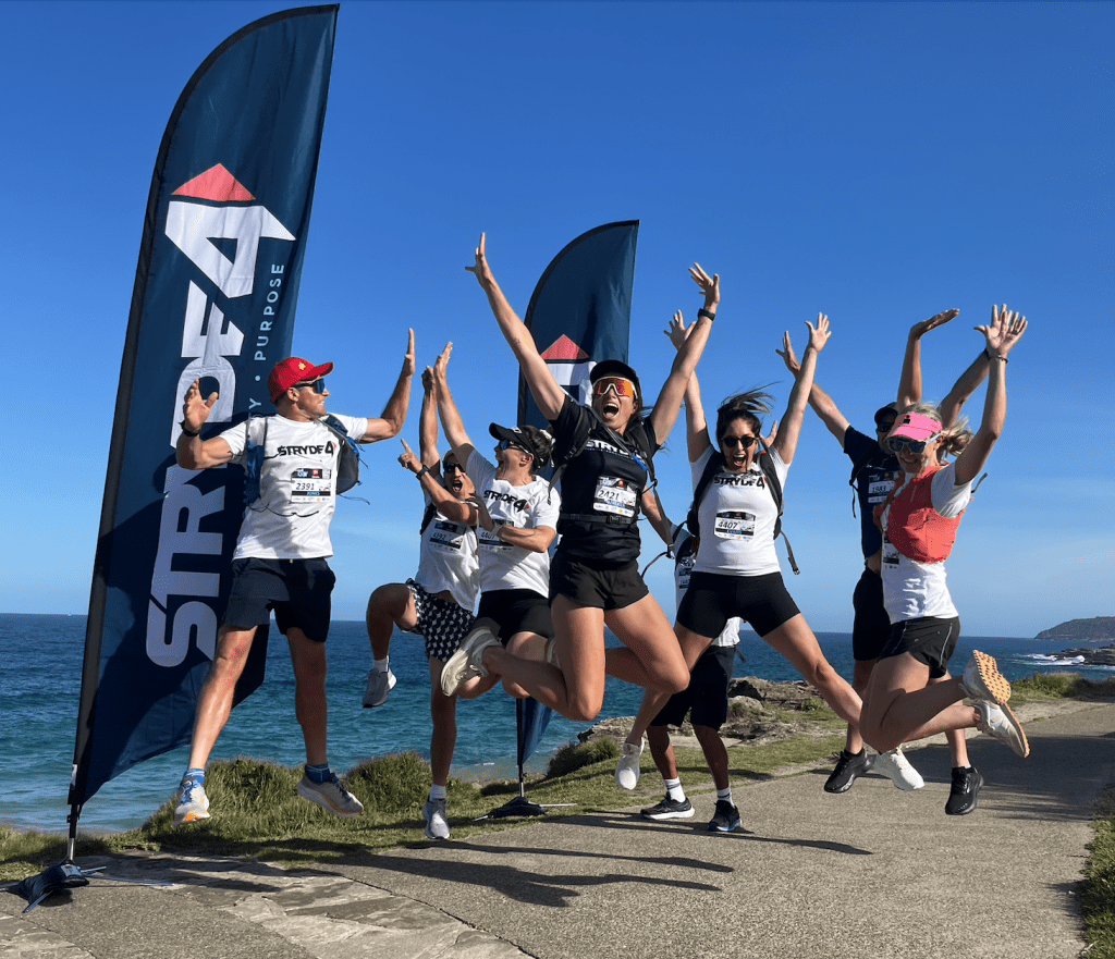 Group of smiling colleagues completing the STRYDE4 Corporate Challenge with charity banners in the background