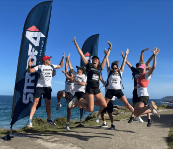 Group of smiling colleagues completing the STRYDE4 Corporate Challenge with charity banners in the background